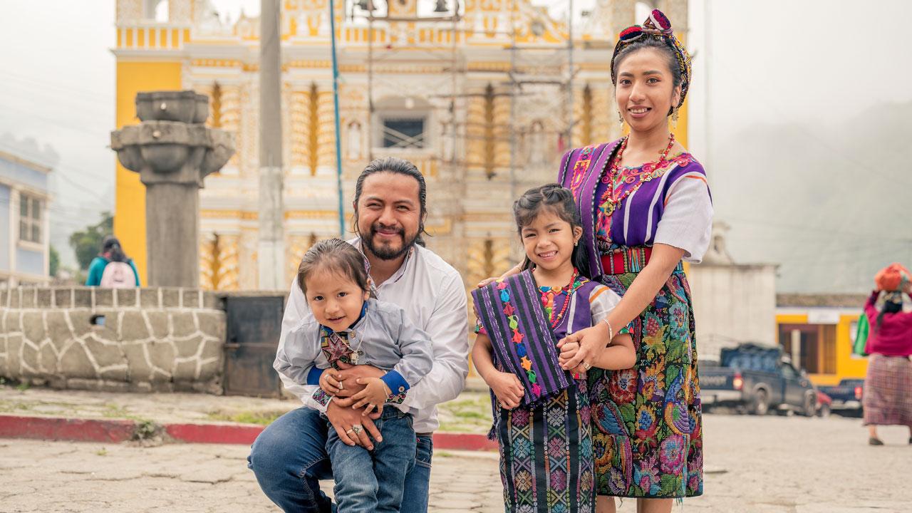 A family in traditional dress poses outdoors in a town square in Guatemala